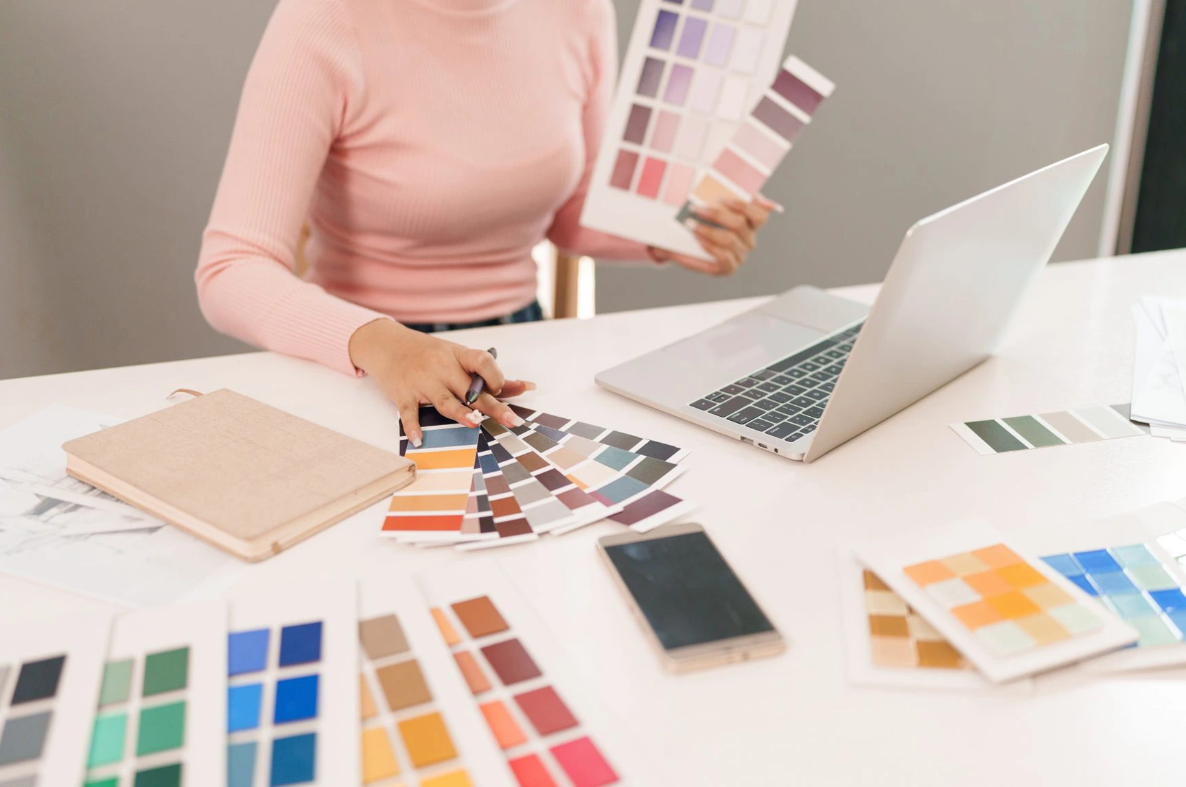 Bildbearbeiterin sitzt an einem Arbeitsplatz mit zwei großen Monitoren und optimiert ein Porträtfoto mithilfe professioneller Retusche-Software; im Hintergrund arbeiten weitere Teammitglieder, was den Prozess hochwertiger Reproduktionen und präziser Bildbearbeitung zeigt.