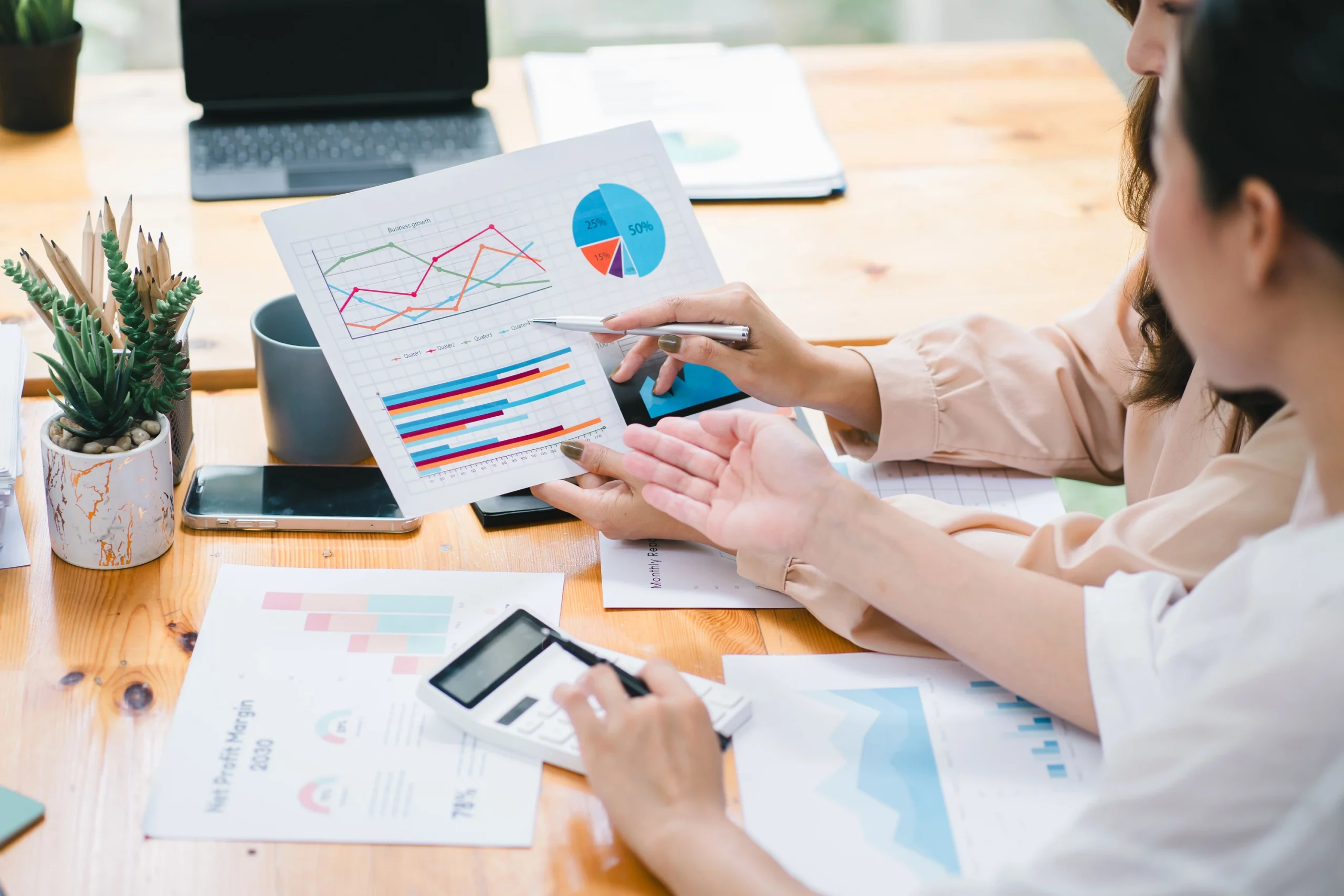 Team bespricht SEO-Daten und Diagramme auf ausgedruckten Reports und einem Tablet; mehrere Hände zeigen auf Kennzahlen wie Traffic-Entwicklung und Ranking-Analysen. Die Szene symbolisiert strategische Suchmaschinenoptimierung, datenbasierte Entscheidungen und kontinuierliche Verbesserung der Online-Sichtbarkeit.