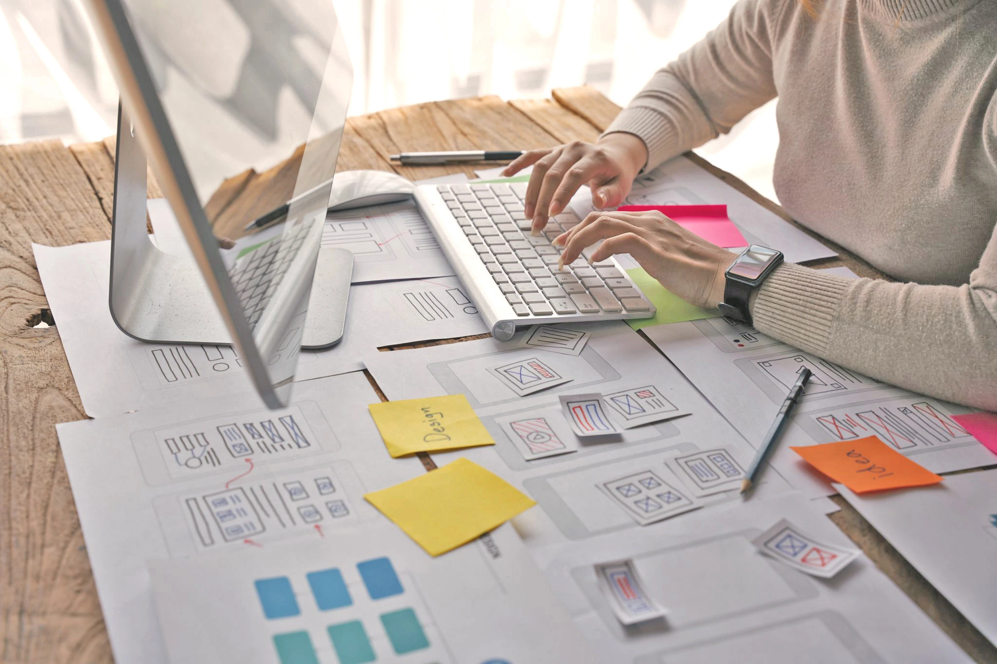 Designer arbeitet am Schreibtisch vor einem Monitor und erstellt digitale Werbebanner; auf dem Tisch liegen Skizzen, Wireframes und farbige Notizzettel für verschiedene Ad-Layouts. Die Szene symbolisiert die kreative Entwicklung von Banner- und Ad-Creatives, die visuell überzeugen und hohe Conversion-Rates erzielen.