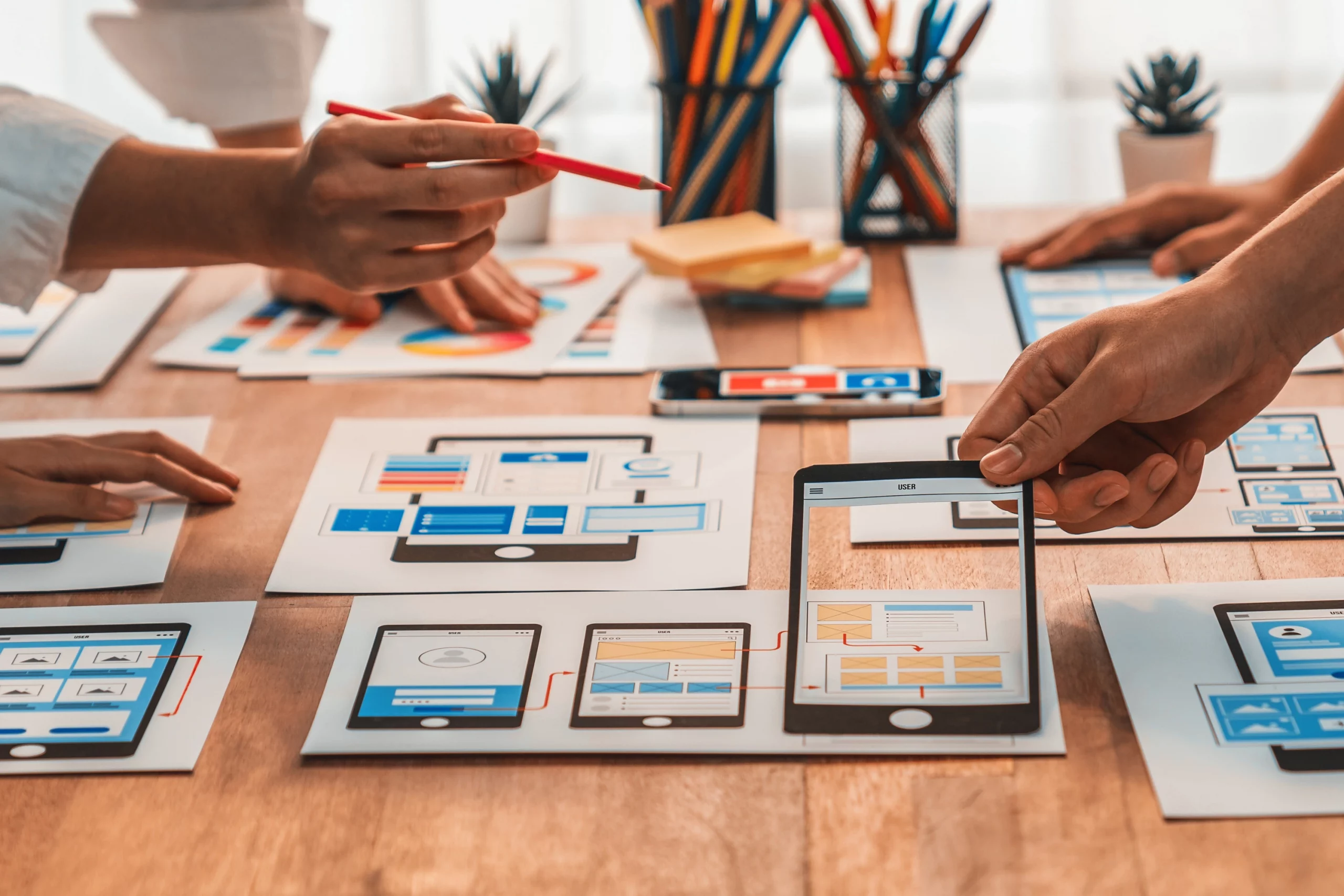 Team arbeitet gemeinsam an digitalen Wireframes und UI-Layouts; Hände zeigen auf Prototypen von Webseiten und Apps, um Design-Konzepte, Nutzerführung und responsives Webdesign für professionelle digitale Projekte abzustimmen.