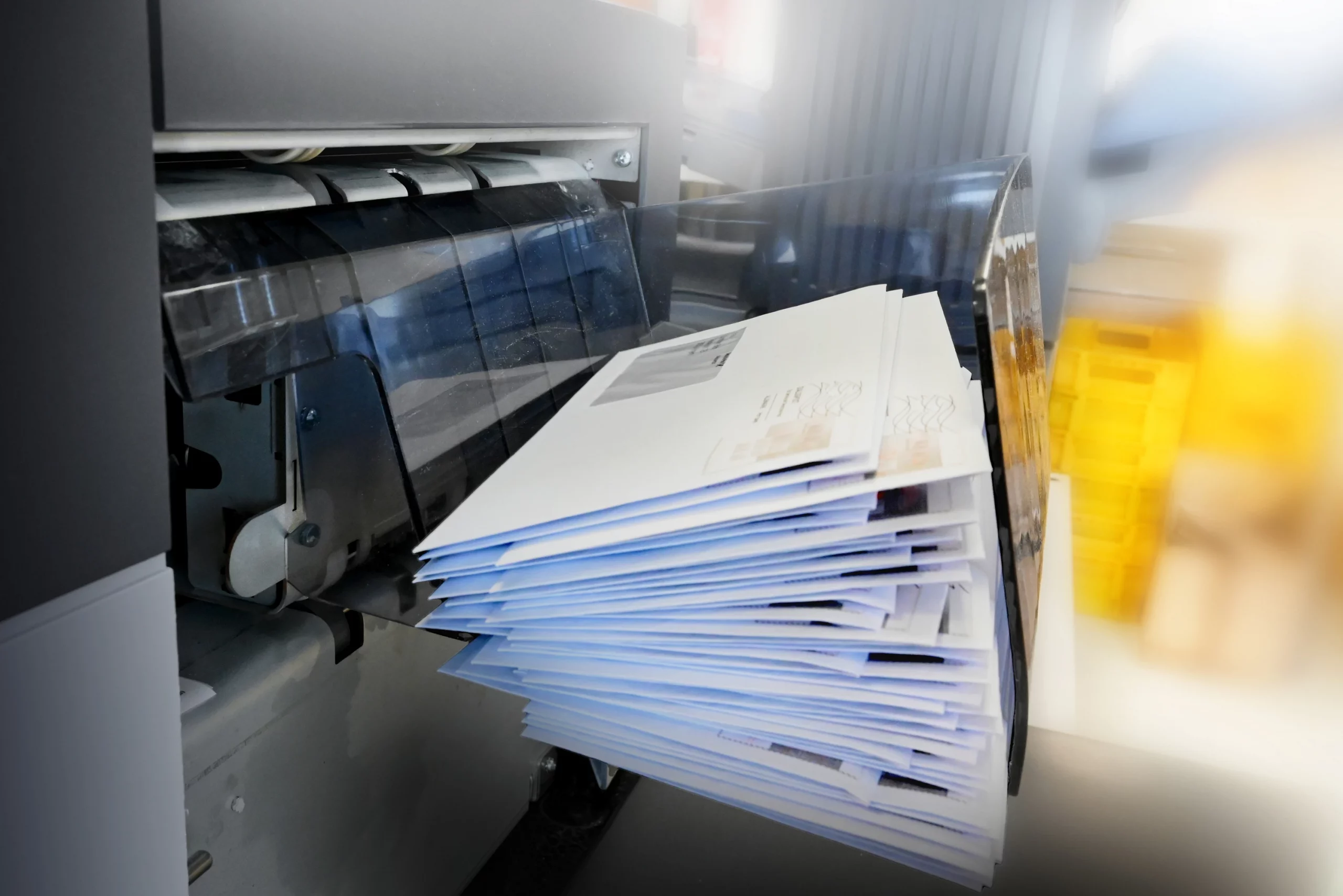 Stapel frisch gedruckter Mailings wird automatisiert aus einer Druckmaschine ausgegeben – zeigt den Lettershop-Prozess mit Kuvertierung, Personalisierung und Versandvorbereitung für Direct-Mail-Kampagnen.
